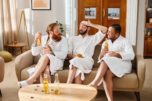 Three diverse, cheerful men in bathrobes enjoy each others company on top of a couch, laughing and bonding. — Stock Photo