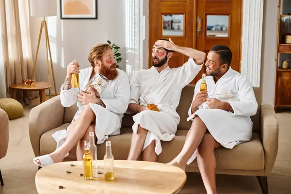 Three diverse, cheerful men in bathrobes enjoy each others company on top of a couch, laughing and bonding. — Stock Photo