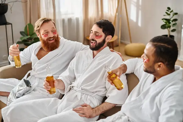 Three diverse, cheerful men in bathrobes enjoying a great time together while sitting on top of a couch. — Stock Photo