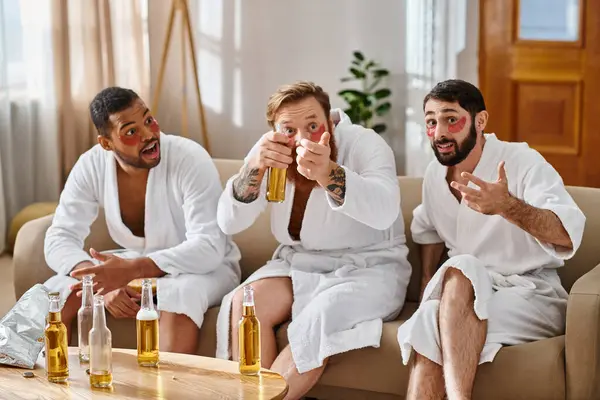 Drei fröhliche, unterschiedliche Männer in Bademänteln sitzen auf einer Couch und teilen Lachen und Kameradschaft. — Stockfoto