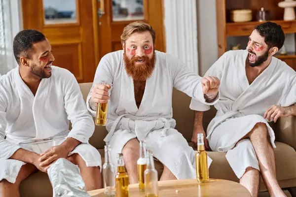 Three diverse cheerful men in bathrobes having a great time lounging and laughing on top of a couch. — Stock Photo