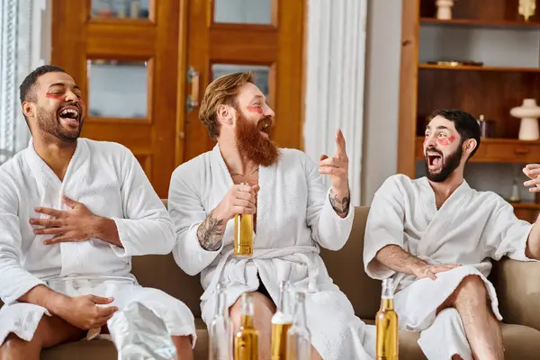 Drei unterschiedliche, gut gelaunte Männer in Bademänteln sitzen auf einer Couch, genießen einander und teilen einen Moment der Kameradschaft. — Stockfoto