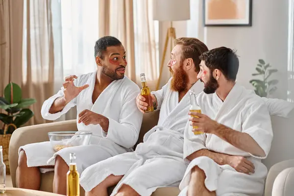 Diversos, homens alegres em roupões de banho relaxando e desfrutando uns dos outros companhia em um sofá luxuoso. — Fotografia de Stock