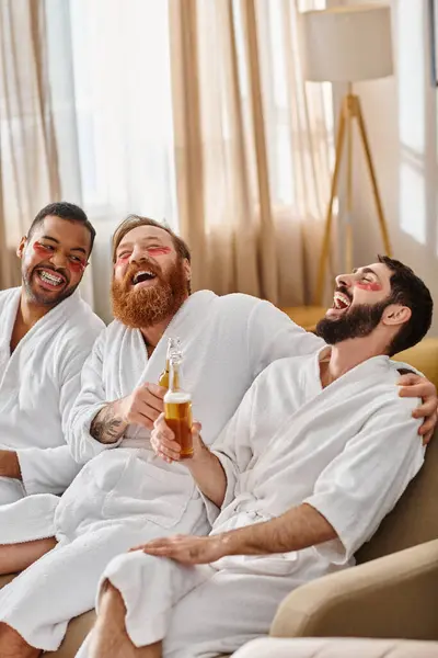 Three diverse, cheerful men in bathrobes having a great time sitting together on a lavish couch. — Stock Photo