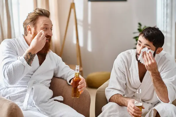 Two cheerful men in bathrobes having a great time sitting on top of a couch and enjoying each others company. — Stock Photo