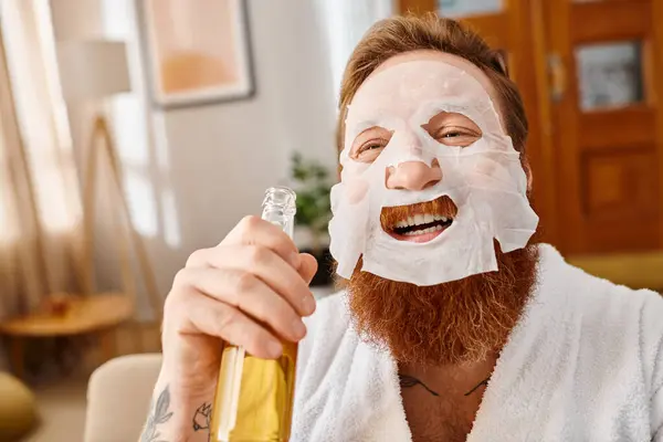 Um homem com uma máscara facial segura uma garrafa de urso e sorri feliz. — Fotografia de Stock