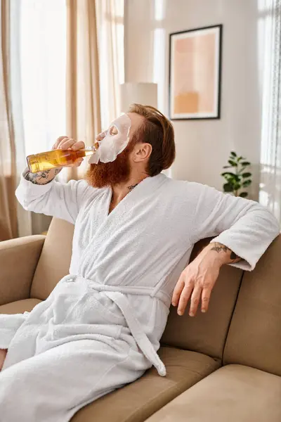 Un uomo in abbigliamento casual si siede comodamente su un divano, sorseggiando tranquillamente una birra. — Foto stock