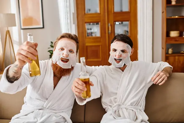 Due uomini in abiti bianchi condividono un momento di divertimento, tenendo in mano la birra e indossando maschere facciali per un momento rilassante e piacevole insieme. — Foto stock