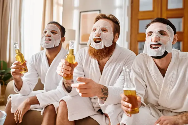 Trois hommes joyeux, divers en arrière-plan, portant des masques faciaux, peignoirs de bain, collant sur la bière. — Photo de stock