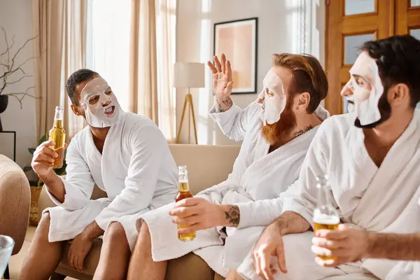 Three diverse cheerful men in bathrobes relaxing and enjoying each others company while sitting on top of a comfortable couch. — Stock Photo