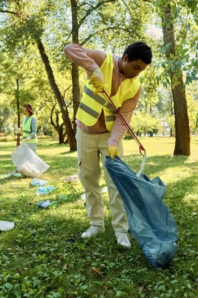 Africano americano homem em uma camisa amarela segura um saco azul contra um fundo vibrante com sua esposa. — Fotografia de Stock