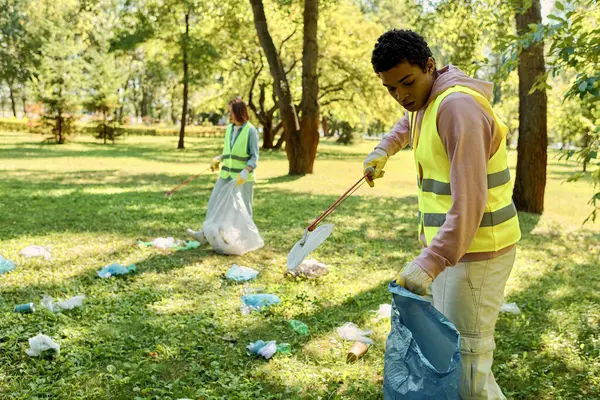 Un couple diversifié vêtu d'un gilet jaune vibrant nettoie l'herbe dans un parc avec soin, incarnant l'esprit de gérance environnementale.. — Photo de stock