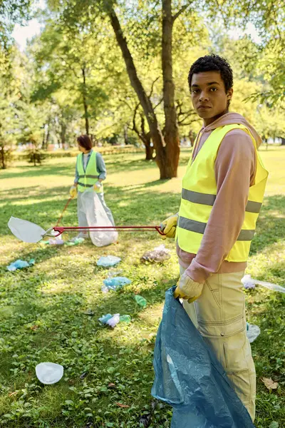 Pareja diversa socialmente activa limpiando un parque juntos. - foto de stock
