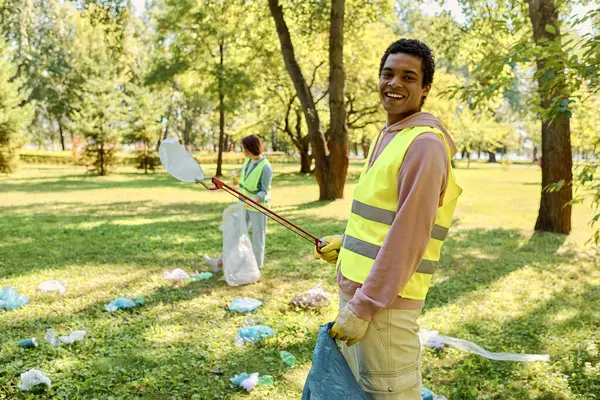 Casal amoroso diversificado socialmente ativo em coletes de segurança e luvas limpando um parque — Fotografia de Stock