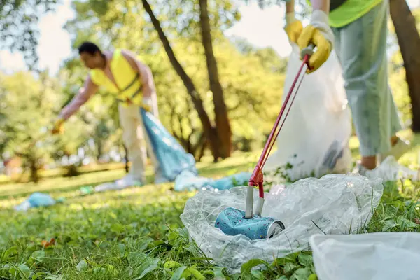 A diverse, harmonious couple in safety vests, gloves, and with a lawn mower, maintaining the parks greenery. — Stock Photo
