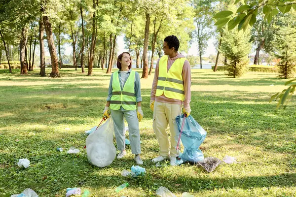 A loving, diverse couple in safety vests and gloves stands united, cleaning a park together. — Stock Photo