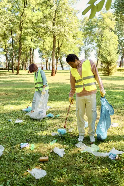 A socially active, diverse couple in safety vests and gloves cleaning a park together, passionate about environmental conservation. — Stock Photo