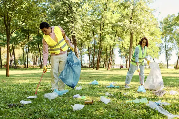 Pareja socialmente activa y diversa que usa chalecos de seguridad y guantes limpiando basura en el parque con un grupo de personas. - foto de stock