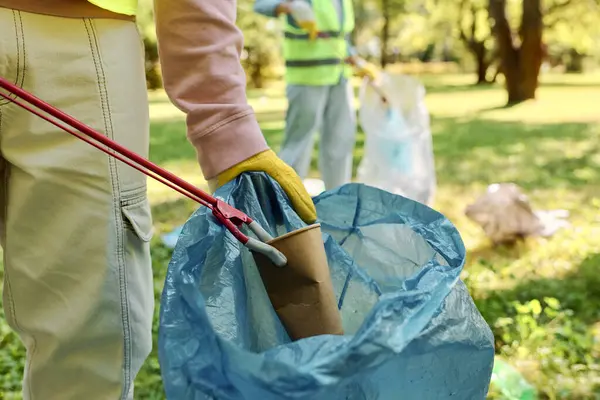 Una persona con un giubbotto di sicurezza e guanti tiene una borsa blu con una maniglia rossa. — Foto stock