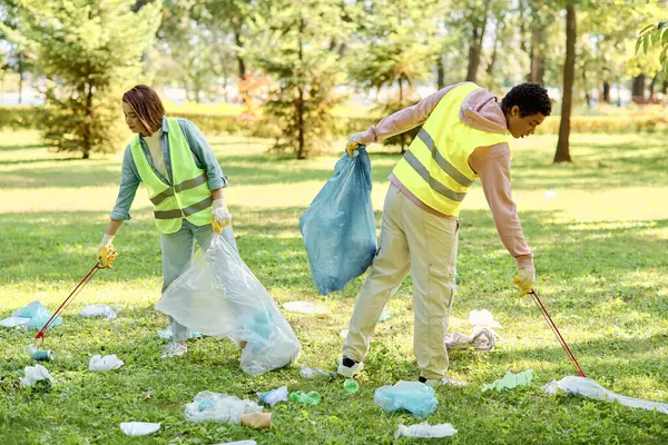 Loving couple in safety vests and gloves standing together in the grass, taking action to clean up the park. — Stock Photo