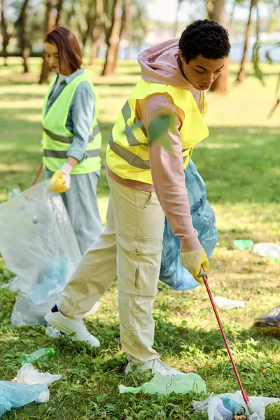 A socially active, diverse loving couple in safety vests and gloves cleaning a lush green park together. — Stock Photo