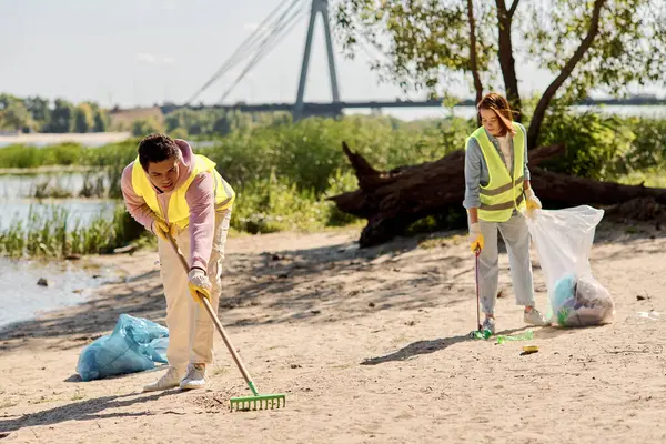 A socially active diverse loving couple in safety vests and gloves, cleaning the park together amidst the serene sandy landscape. — Stock Photo