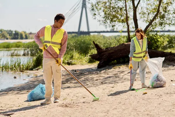 Социально активная пара в защитных жилетах и перчатках, объединенная в усилиях по охране окружающей среды, стоит на песке. — стоковое фото