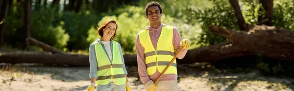 A diverse, socially active couple, in safety vests and gloves, standing together in dirt, cleaning a park with care. — Stock Photo