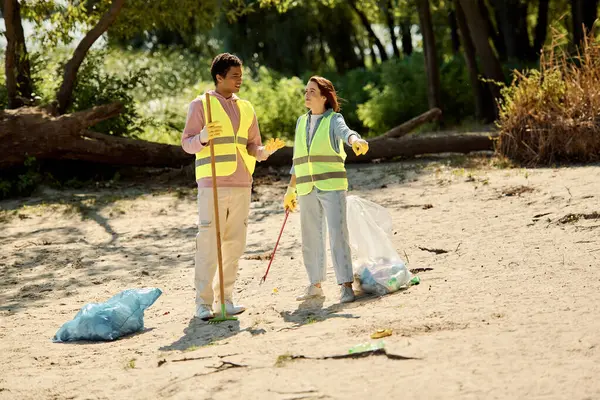 A man and a woman, a socially active diverse loving couple, clean a beach wearing safety vests and gloves. — Stock Photo