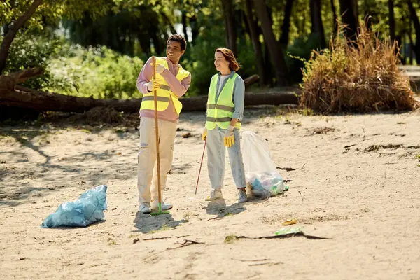 Um casal socialmente ativo em coletes de segurança e luvas limpa a praia de areia juntos, garantindo um ambiente mais seguro para todos. — Fotografia de Stock