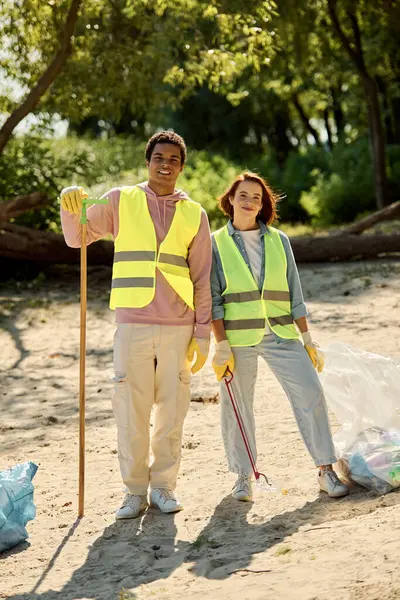 A socially active diverse couple, adorned in safety vests and gloves, stands united on the beach. — Stock Photo