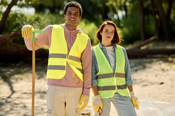 A socially active, diverse couple in safety vests and gloves stand side by side, committed to cleaning up the park together. — Stock Photo