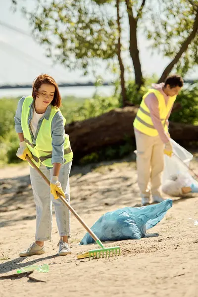 A socially active, diverse loving couple in safety vests and gloves are seen cleaning a beach together, removing litter and debris. — Stock Photo