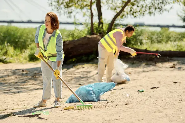 Una pareja amorosa, con chalecos y guantes de seguridad, de pie en la arena, limpiando un parque juntos para preservar el medio ambiente. - foto de stock