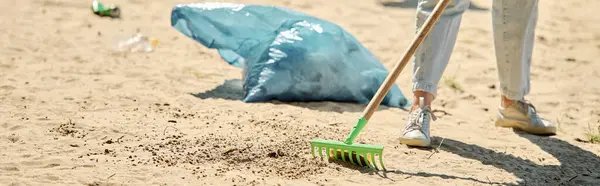 Una pala y una bolsa de polvo se colocan en una playa, mostrando las herramientas de una pareja socialmente activa limpiando el medio ambiente juntos. - foto de stock