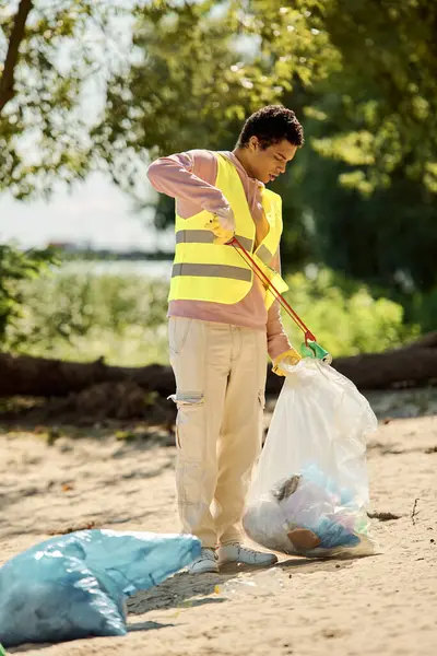 Un hombre está parado a lo largo de la costa, sosteniendo una bolsa de plástico, contemplando el impacto ambiental de la basura en nuestras playas. - foto de stock