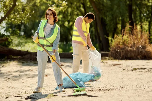 A socially active diverse couple in safety vests and gloves standing in the sand, cleaning the park together. — Stock Photo