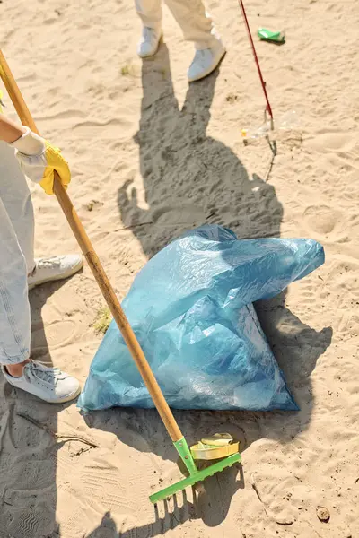 Una persona con una pala y una bolsa en la playa, limpiando y cuidando el medio ambiente. - foto de stock