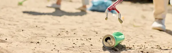 Освіжаюча банка содової, що відпочиває на піщаному пляжі під сонцем тепле сяйво, в той час як різноманітна пара прибирає пляж. — стокове фото
