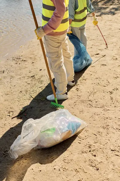 Una coppia eterogenea si trova su una spiaggia sabbiosa, unita nella loro cura per l'ambiente mentre puliscono insieme.. — Foto stock