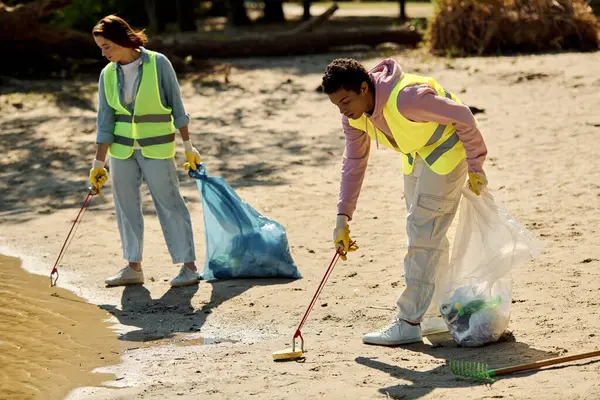 Couple in safety vests & gloves working together in the sand at the park. — Stock Photo
