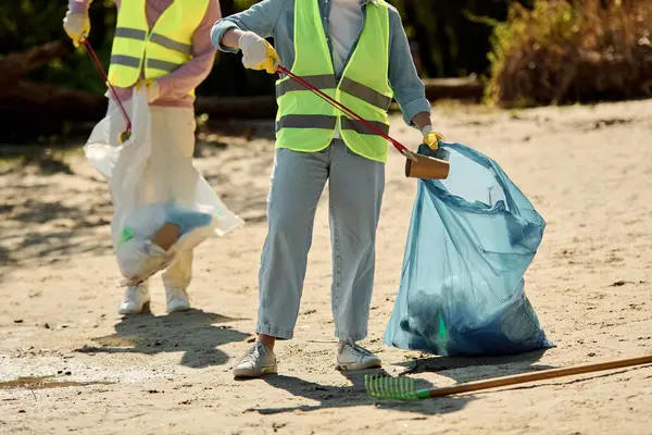 A couple in safety vests and gloves stands in the sand, united in cleaning a park together. — Stock Photo