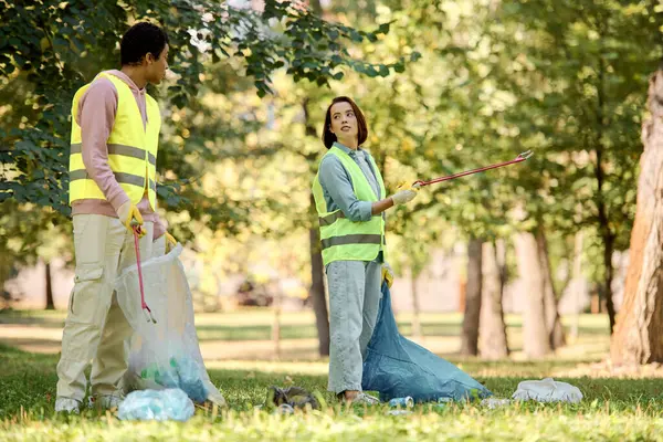 Ein vielseitiges Paar in Sicherheitswesten und Handschuhen, das mit Liebe und Hingabe einen Park säubert. — Stockfoto