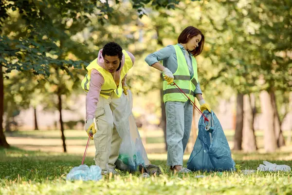 Ein liebevolles, vielfältiges Paar in Sicherheitswesten und Handschuhen steht im Gras und säubert gemeinsam den Park.. — Stockfoto