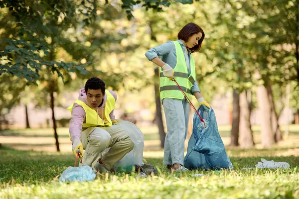 Ein sozial aktives, vielfältiges Liebespaar in Warnwesten und Handschuhen säubert fleißig das Gras im Park. — Stockfoto