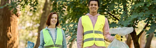 A socially active, diverse couple wearing safety vests and gloves, lovingly cleaning a park together. — Stock Photo