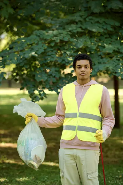 African american man in a yellow vest holding a bag of garbage. — Stock Photo