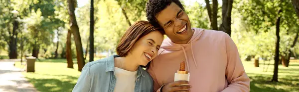Un homme et une femme en tenue vibrante partagent joyeusement une bouteille de bière dans un parc, profitant mutuellement de la compagnie. — Photo de stock