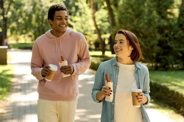 Разнообразная, любящая пара, идущая по живописному тротуару в яркой одежде, наслаждаясь компанией друг друга. — стоковое фото