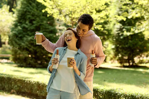 A stylish couple in vibrant attires enjoying coffee together in a park, creating a heartwarming scene. — Stock Photo